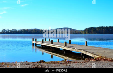 Dock di legno che si estendono oltre il lago di acqua. Bella immagine serena di molo in legno con acque blu e blu del cielo, lontane colline in background. Foto Stock