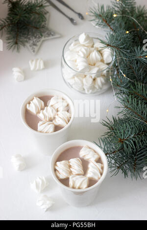 Il cacao con marshmelow in bianco tazze e marshmallows in un vasetto di vetro su un tavolo bianco con rami di abete rosso, una ghirlanda di fiori e una stella bianca. Messa a fuoco selettiva Foto Stock