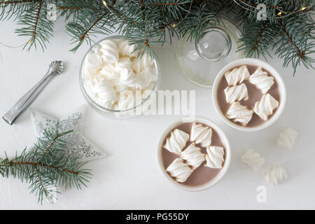 Il cacao con marshmelow in bianco tazze e marshmallows in un vasetto di vetro su un tavolo bianco con rami di abete rosso, una ghirlanda di fiori e una stella bianca. Messa a fuoco selettiva Foto Stock