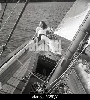 1940s barca a vela. Una giovane donna è a bordo di un quartiere alla moda di barca a vela ed è giacente sul ponte quando e crociere in avanti con il vento nelle vele. Indossa un tipico degli anni quaranta moda. La Svezia 1946 Photo Kristoffersson ref AC102-2 Foto Stock