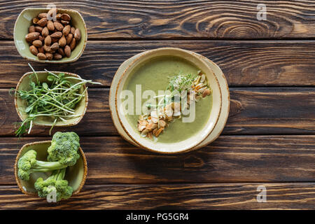 Vista superiore del disposto vegetariana minestra di crema, germogli, mandorle e broccoli freschi in ciotole su una superficie di legno Foto Stock