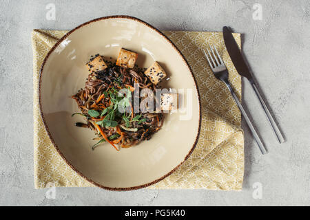 Composizione alimentare con soba con tofu e verdure decorate con semi germinati di girasole sul piano portapaziente grigio Foto Stock