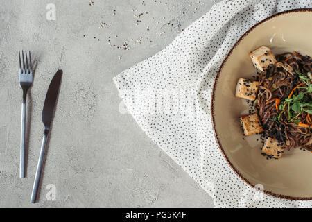 Composizione alimentare con soba con tofu e verdure decorate con semi germinati di girasole sul piano portapaziente grigio Foto Stock