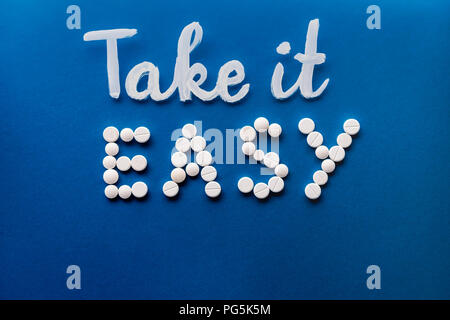 Vista superiore del lettering take it easy realizzato da pillole di bianco su sfondo blu Foto Stock