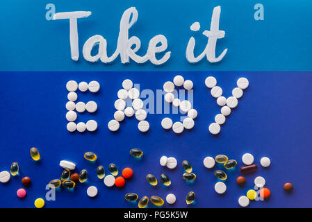 Vista superiore del lettering take it easy da pillole di bianco vicino a varie pastiglie su sfondo blu Foto Stock