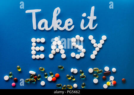 Vista superiore del lettering take it easy realizzato da pillole di bianco vicino a varie pastiglie su sfondo blu Foto Stock