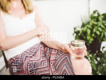 Donna bionda rilassante sul patio holding bevanda ghiacciata Foto Stock