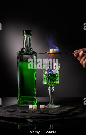 Ritagliato colpo di donna holding cucchiaio con cubetti di zucchero oltre la masterizzazione di assenzio in vetro su sfondo scuro Foto Stock