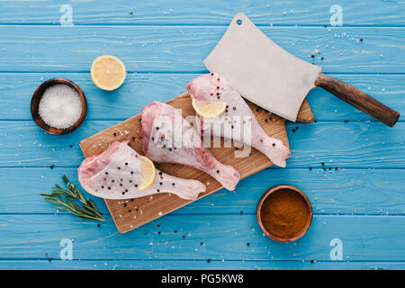 Vista superiore di materie le cosce di pollo su tavola di legno con spezie e cleaver sul piano portapaziente blu Foto Stock