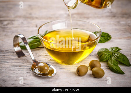 Bottiglia versando olio d'oliva vergine in una ciotola close up Foto Stock