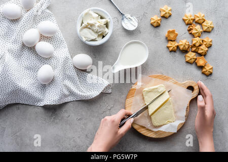 Ritagliato colpo di donna burro di taglio sul tagliere per fatta in casa torta sul tavolo grigio Foto Stock