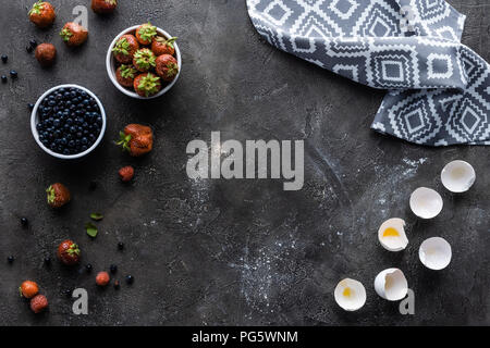 Lay piatto con frutti di bosco freschi, uova e biancheria in grigio scuro superficie Foto Stock