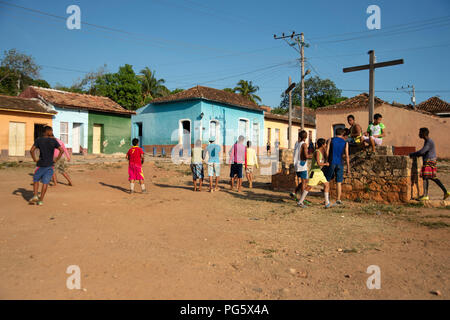 Gli adolescenti cubani a giocare il gioco del calcio sulla massa di rifiuti in Trinidad con casa tradizionale in background Foto Stock