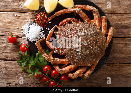 Lussuoso materie granseola circondato da pomodori freschi, limone, le erbe aromatiche e le spezie close-up su una pietra nera. Parte superiore orizzontale vista da sopra Foto Stock