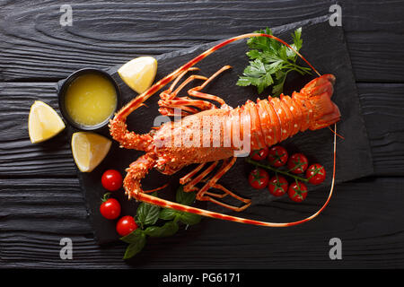 Cibi costosi: spinoso aragosta bollita con pomodoro fresco, succo di limone e il burro fuso close-up sulla pietra nera. Parte superiore orizzontale vista da sopra Foto Stock