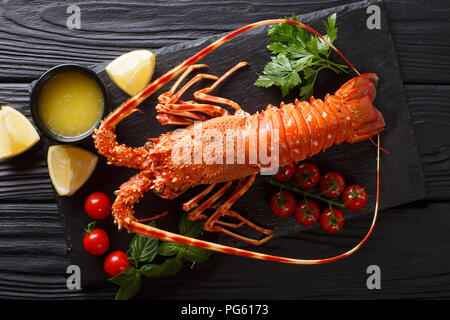 Lussuoso bollito di aragosta circondato da pomodori freschi, limone, erbe aromatiche e burro fuso close-up su una pietra nera. parte superiore orizzontale vista da sopra Foto Stock