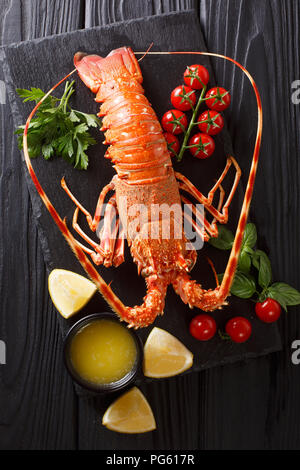 Cibi costosi: spinoso aragosta bollita con pomodoro fresco, succo di limone e il burro fuso close-up sulla pietra nera. Verticale in alto vista da sopra Foto Stock