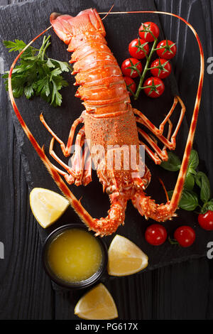 Cibo delizioso: bollito o spinoso rocky astice con pomodoro, limone e il burro fuso close-up su una scheda di colore nero. Verticale in alto vista da sopra Foto Stock