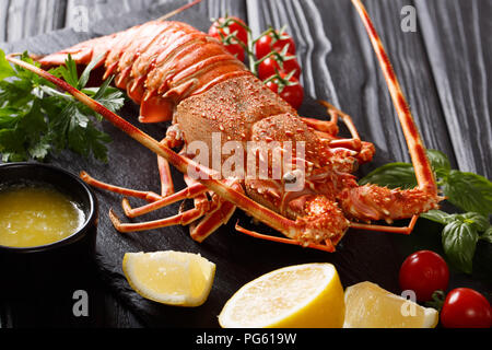 Ristorante sano cibo bollito di aragosta gamberi con pomodori freschi, limone, erbe aromatiche e burro fuso close-up su uno sfondo nero. orizzontale Foto Stock