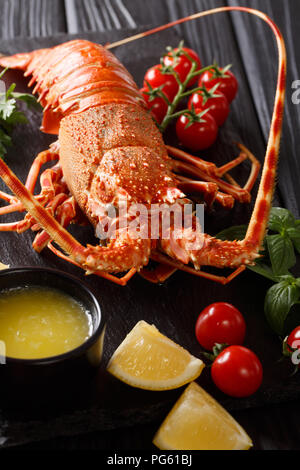 Cibo delizioso: bollito o spinoso rocky astice con pomodoro, limone e il burro fuso close-up su una lavagna nera verticale. Foto Stock