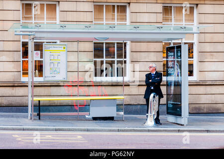 Un musicista con la sua tuba in attesa ad una fermata di autobus di Newcastle, England, Regno Unito Foto Stock