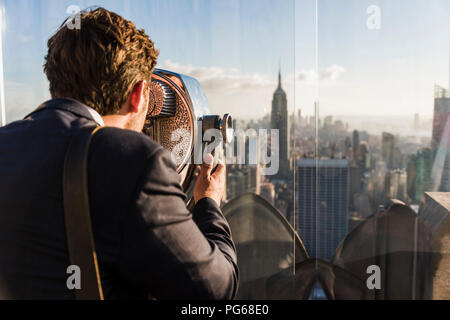 Stati Uniti d'America, New York City, l'uomo cerca attraverso la gettoniera binocolo sul Rockefeller Center observation deck Foto Stock