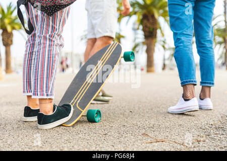 Close-up di amici con uno skateboard su un lungomare con palme Foto Stock