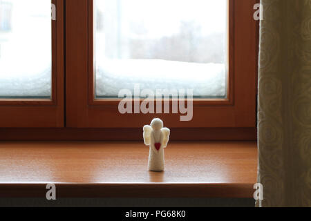 Giocattolo di lana angelo in piedi su un davanzale contro una finestra nevoso Foto Stock