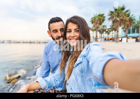 Spagna, Barcellona, sorridente giovane prendendo un selfie al mare Foto Stock