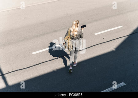 Giovane Donna che cammina sulla strada vuota, parlando in il suo smartphone Foto Stock