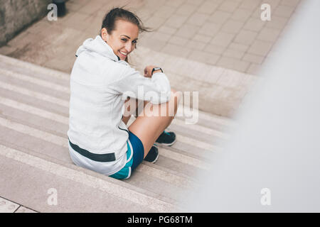 Sorridente sportive giovane donna seduta sulle scale all'aperto Foto Stock