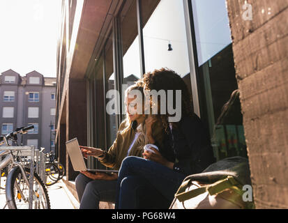 Gli amici seduti davanti alla finestra nella città, utilizzando laptop Foto Stock