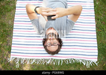 Uomo disteso sulla coperta in un parco tramite telefono cellulare, vista dall'alto Foto Stock