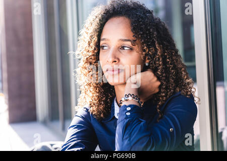 Giovane donna seduta di fronte alla finestra nella città, ritratto Foto Stock