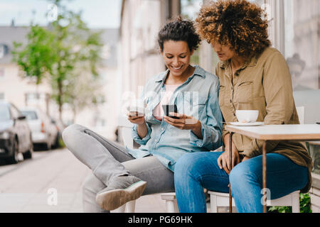 Due amici che lavorano in coworking space, seduta a tavola con caffè, utilizza lo smartphone Foto Stock