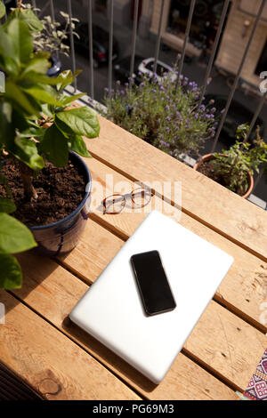 Smartphone, laptop e occhiali sulla tavolozza sul balcone Foto Stock