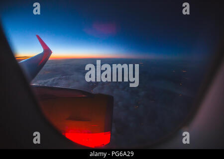 Vista attraverso un oblò sull'ala di un aeroplano e una turbina giallo all'alba nuvole cloud Foto Stock