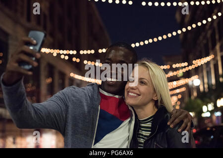 Felice giovane uomo con la fidanzata prendendo un selfie di notte Foto Stock