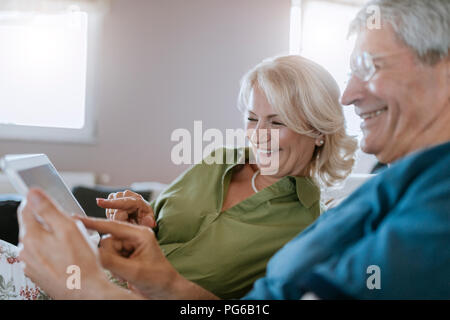 Felice coppia senior a casa seduti sul lettino usando tablet Foto Stock