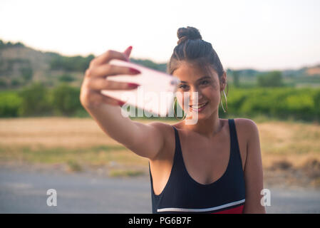 Ritratto di sorridente ragazza adolescente tenendo selfie con lo smartphone all'aperto Foto Stock