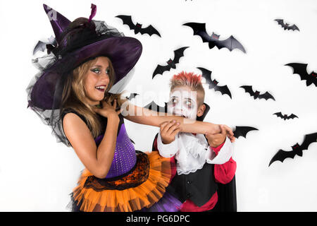 Bambini festeggiare Halloween in costume di strega e vampiro. Vampire finge di morso della strega e braccio sorride in risposta. Foto Stock