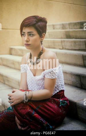 Bella giovane donna sat sui gradini all'aperto che guarda lontano Foto Stock