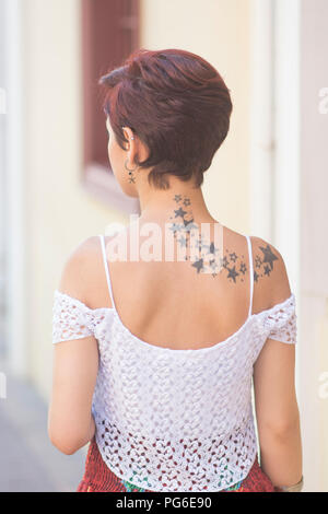 Vista posteriore di una giovane donna con corti capelli rossi e stelle tatuaggio sul retro all'esterno permanente Foto Stock
