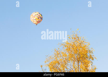 La mongolfiera in un cielo blu. Mongolfiera galleggiante sopra un albero in autunno, Derbyshire, England, Regno Unito Foto Stock