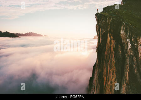 Traveler permanente sulla scogliera di bordo superiore di montagna sopra le nuvole al tramonto avventuroso viaggio lifestyle estate vacanze viaggio Foto Stock