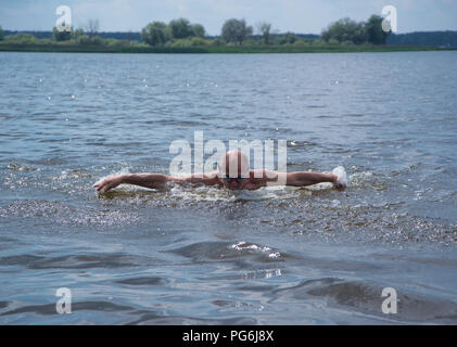 Un anziano uomo muscolare in occhiali da nuoto nuota con una farfalla stile, vista frontale Foto Stock