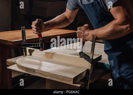 Ritagliato colpo di falegname in grembiule lavorando su legno in officina Foto Stock