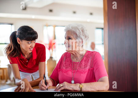 Senior donna firma un contratto, infermiere aiutandola Foto Stock