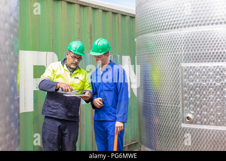 Lavoratore con la compressa a contenitore parlando di co-lavoratore Foto Stock