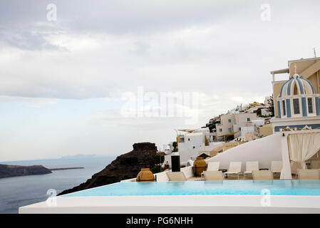 Piscina infinity e torre campanaria a strisce sulla caldera di Santorini, Grecia. Foto Stock